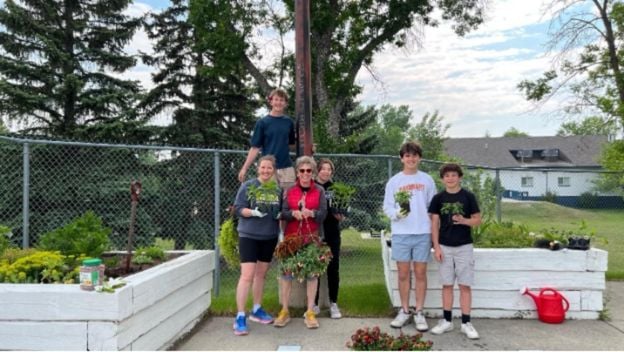 A small group of 6 people gathered in front of 2 white recently-planted planter boxes